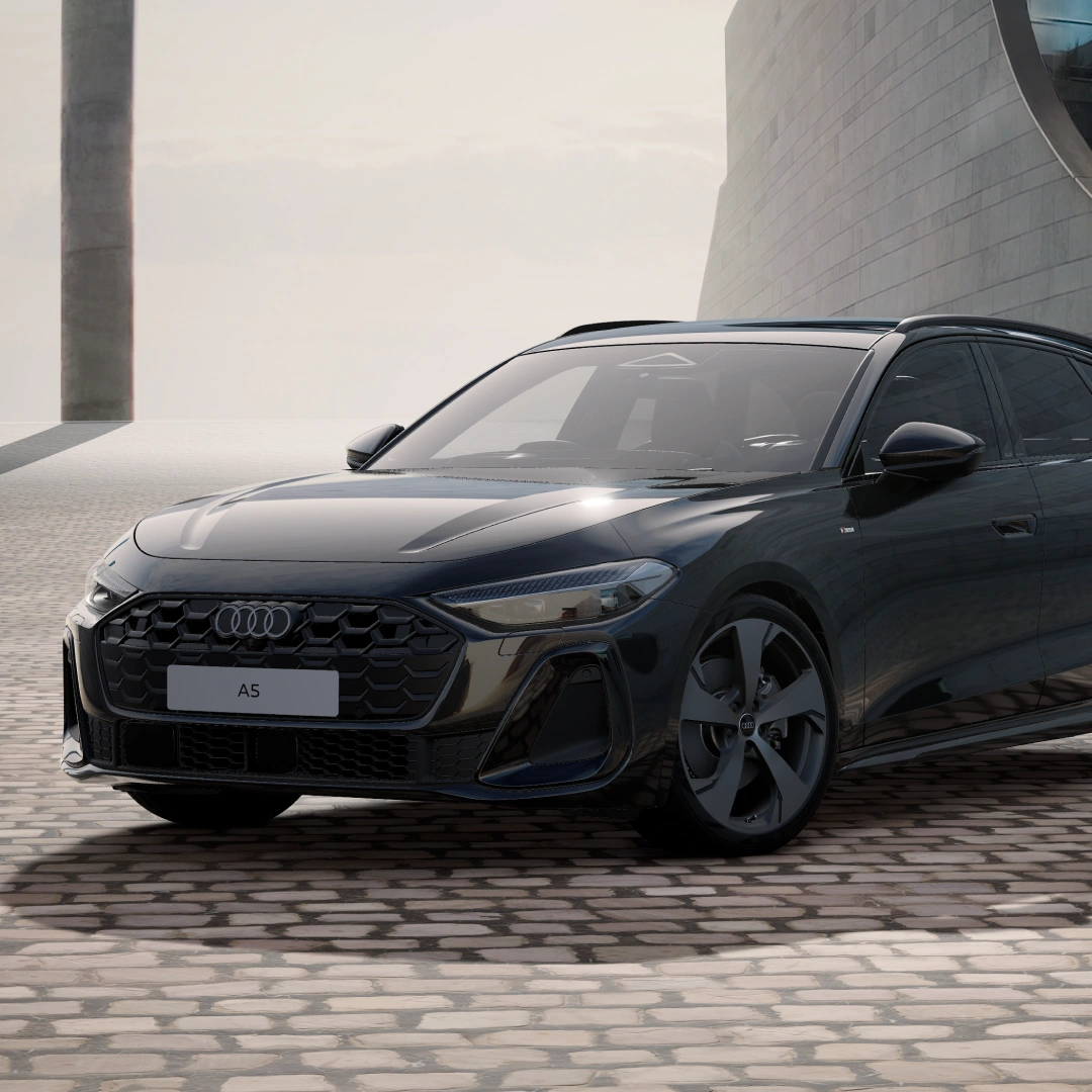 Front three-quarter view of a black Audi A5 Avant parked in a contemporary architectural setting, showcasing the Audi Singleframe grille, LED headlights, alloy wheels and sporty estate design.